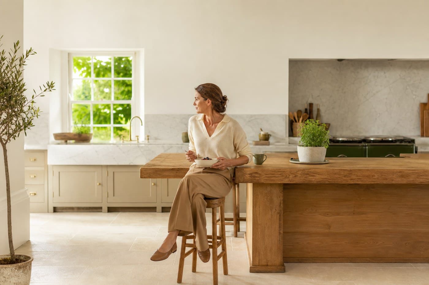 A woman in her late forties at a kitchen counter in daylight, one hand at her middle, calm and ordinary.