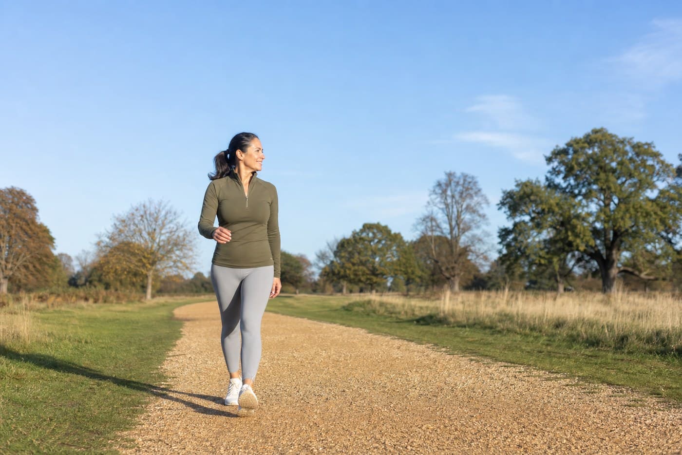 A woman around fifty walking briskly outdoors in daylight in ordinary clothes.